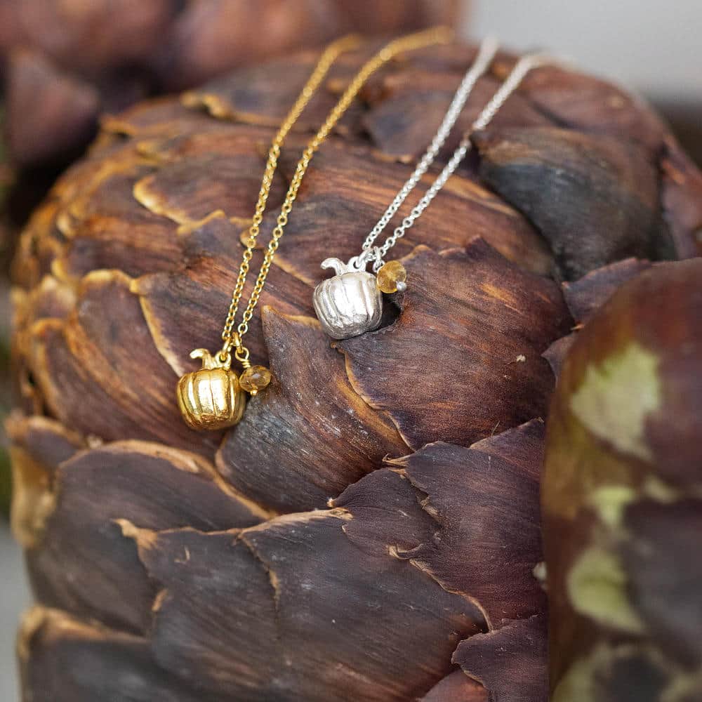 Gold and silver pumpkin necklaces with small gemstone charms, styled on a rustic artichoke background