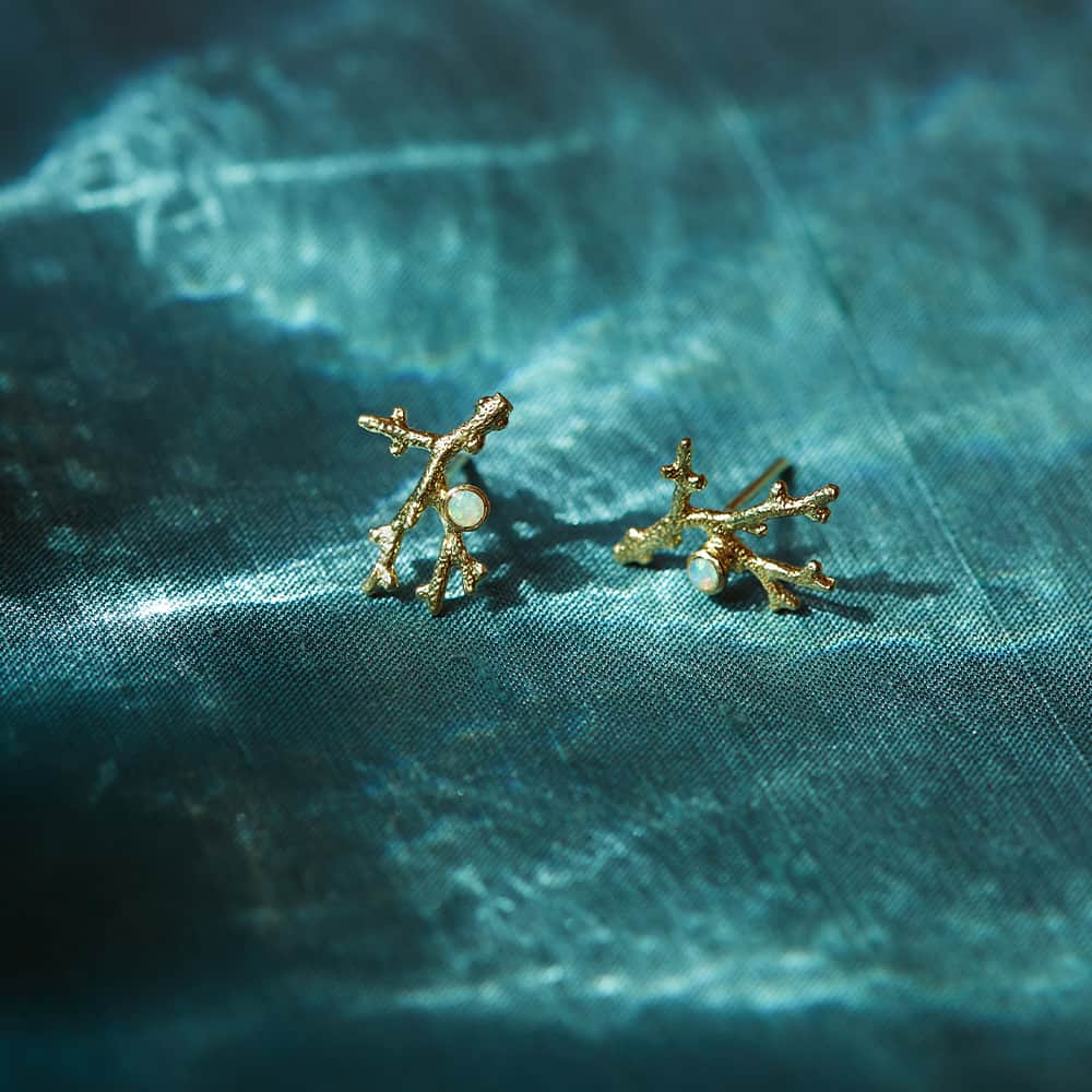 Gold shell pendant necklace and coral-inspired stud earrings with opal gemstones, styled on a white dish with loose opals