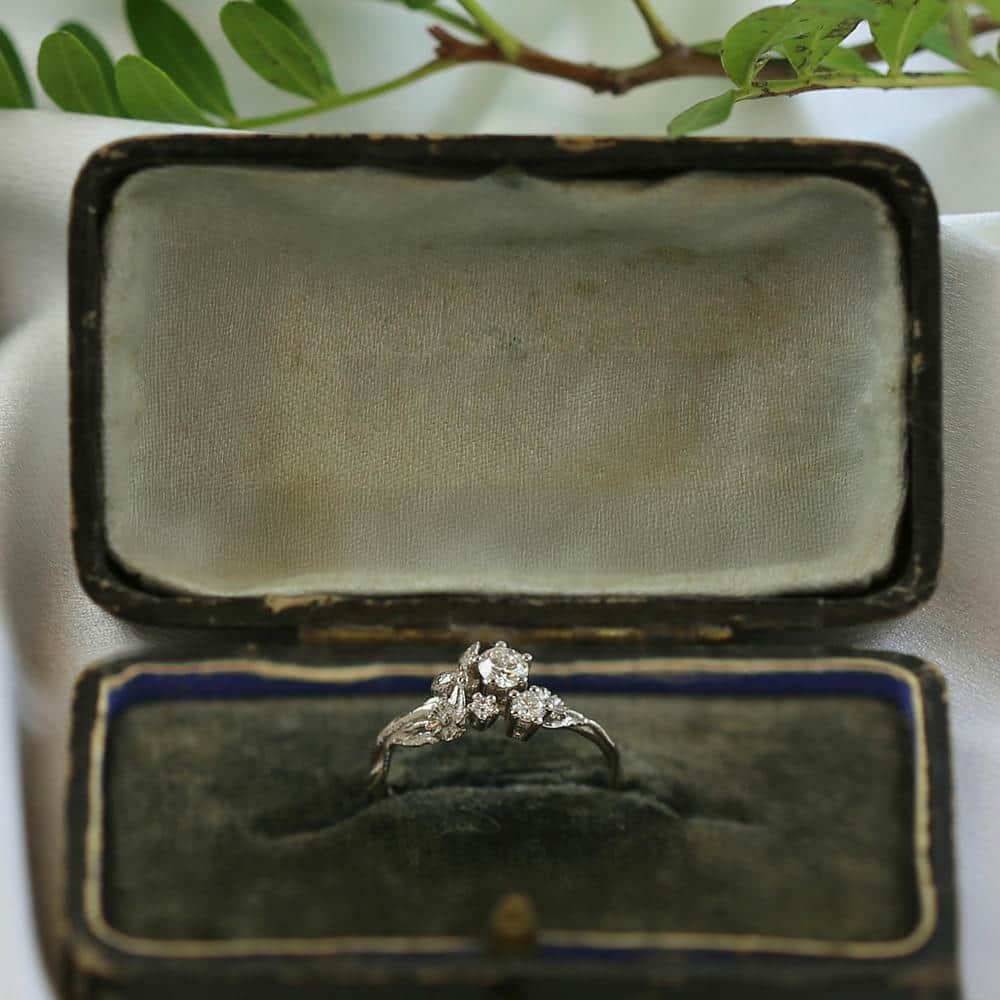 Three gold engagement rings with intricate floral detailing and sparkling central stones, displayed on a rolled cream napkin with a green flower in the background